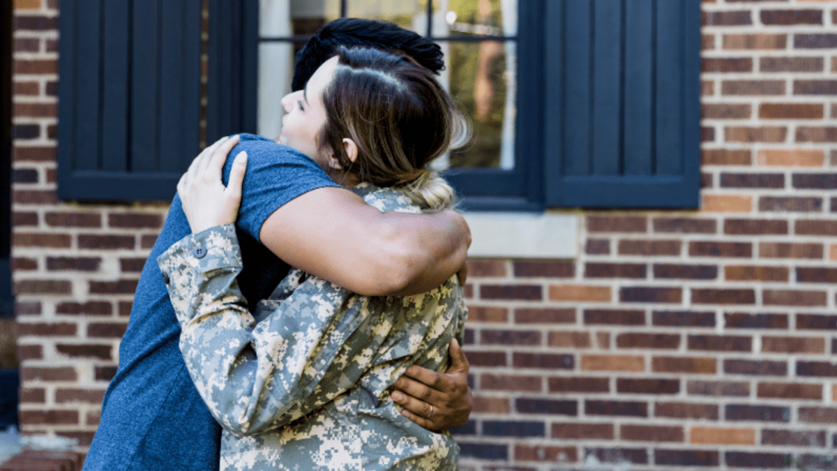 Man hugging spouse who is a woman in military uniform