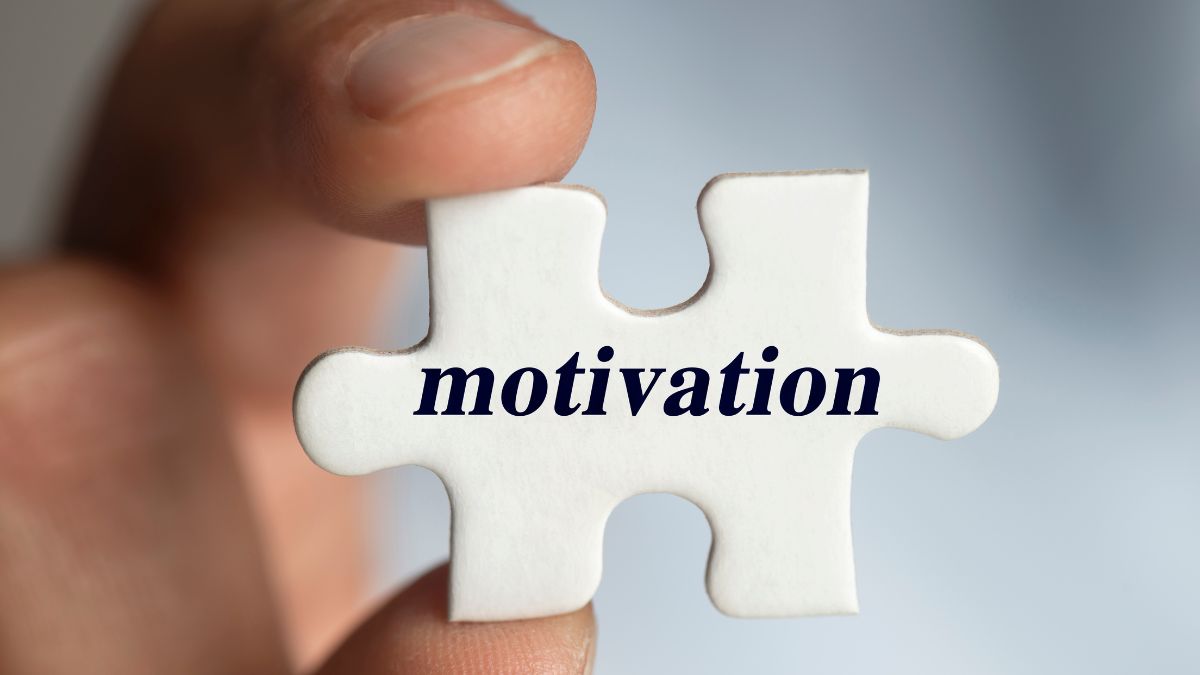White puzzle piece with word "motivation" on it being held by thumb and first finger