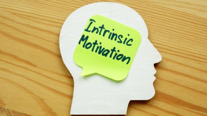 Cutout of the shape of a head with a sticky note on top in the shape of a speech bubble with the words Intrinsic Motivation on it