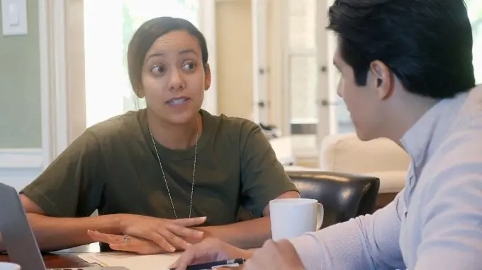 Woman in military uniform shirt wearing dog tags talking to her husband at the table.