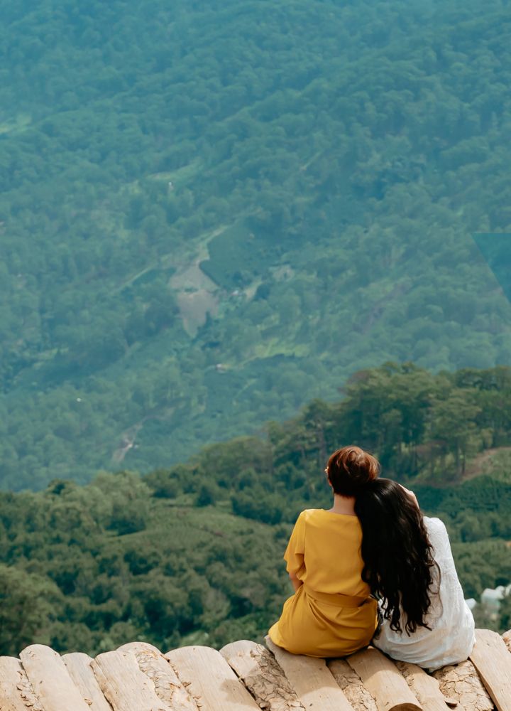 two friends sitting on an edge looking at a forst